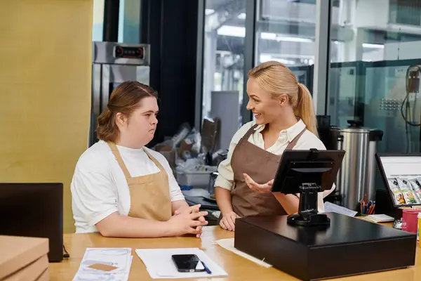 Administrateur de café souriant montrant terminal de trésorerie à la jeune femme avec le syndrome du duvet, inclusivité — Photo de stock