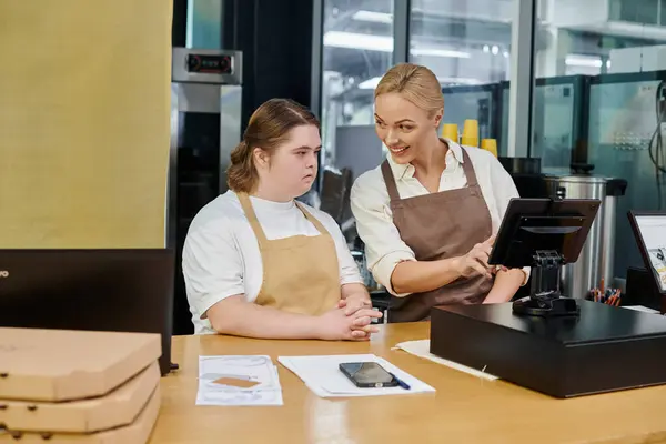 Positive cafe administrator operating cash terminal near young woman with down syndrome, inclusivity — Stock Photo