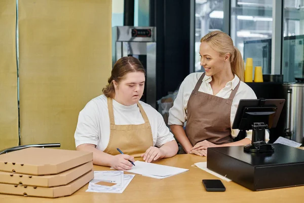Mujer joven con trastorno mental orden de escritura cerca de administrador positivo y cajas de pizza en la cafetería - foto de stock