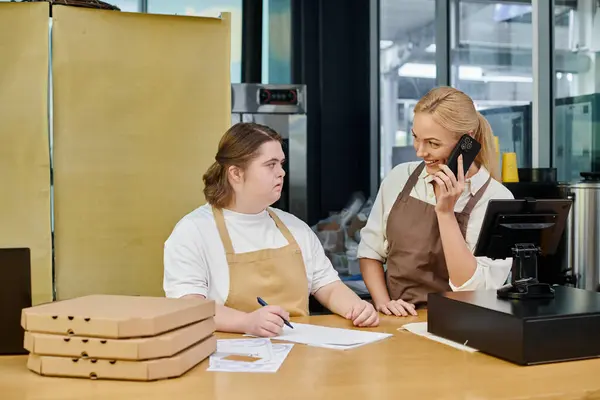 Gerente alegre falando no smartphone perto do empregado feminino com síndrome de down no café moderno — Fotografia de Stock