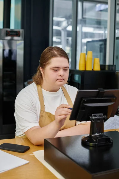 Jeune femme avec syndrome duvet opérant terminal de trésorerie sur le comptoir dans un café moderne, inclusivité — Photo de stock
