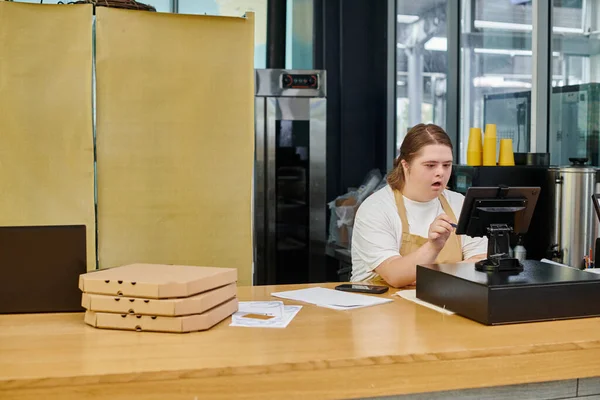 Mulher surpreso com síndrome de down olhando para terminal de dinheiro perto de caixas de pizza no café moderno — Fotografia de Stock