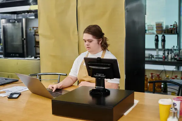 Jovem funcionária com síndrome de down trabalhando com laptop e terminal de dinheiro no balcão no café — Fotografia de Stock