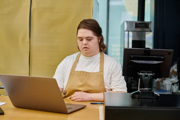 Junge Mitarbeiterin mit geistiger Störung arbeitet am Laptop in der Nähe des Geldautomaten am Schalter im Café — Stockfoto