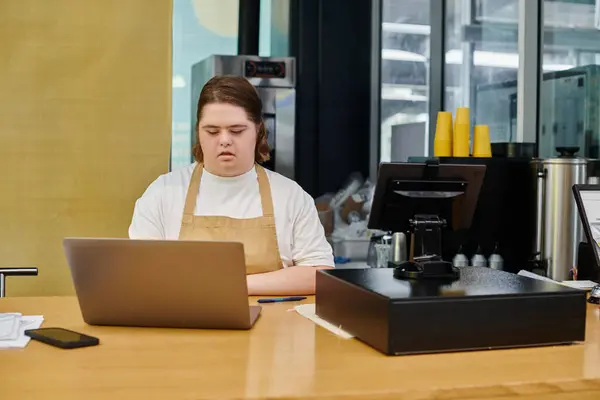 Employée concentrée ayant une déficience mentale travaillant sur un ordinateur portable près d'un terminal de caisse dans un café moderne — Photo de stock