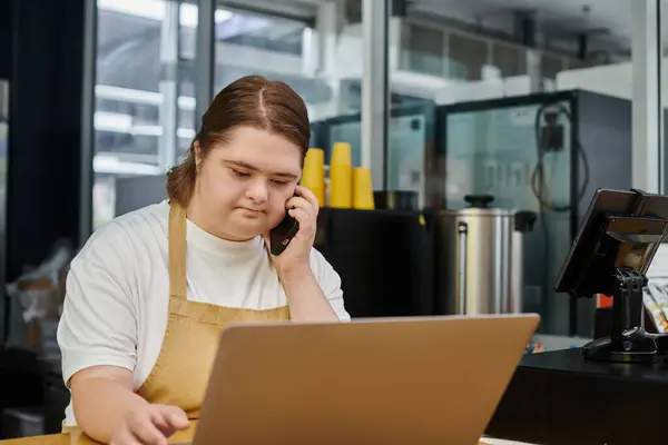 Female employee with down syndrome talking on smartphone near laptop while working in modern cafe — Stock Photo