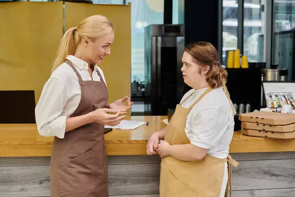 Positive administrator talking to young female employee with down syndrome at counter in modern cafe — Stock Photo
