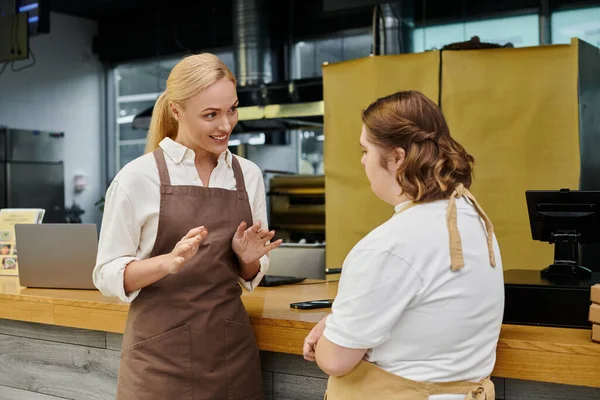 Cheerful administrator explaining duties to young woman with down syndrome at counter in cafe — Stock Photo