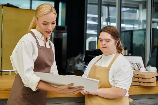 Administratrice de café montrant le carnet de commandes à une jeune employée atteinte du syndrome du duvet, inclusivité — Photo de stock
