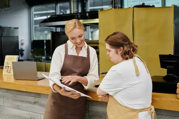 Manager caffè sorridente mostrando portafoglio ordini a giovane dipendente donna con sindrome di Down, inclusività — Foto stock