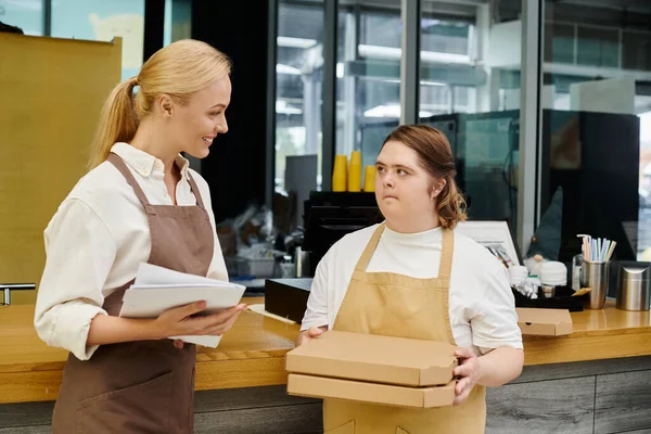 Mujer joven con discapacidad mental sosteniendo cajas de pizza cerca del gerente sonriente en la cafetería moderna - foto de stock