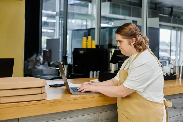 Young female employee with down syndrome working on laptop on counter in cafe, inclusivity — Stock Photo