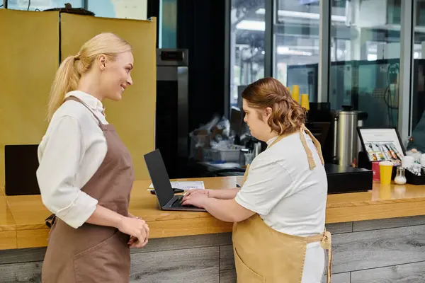 Smiling administrator looking at female employee with down syndrome working on laptop in cafe — Stock Photo