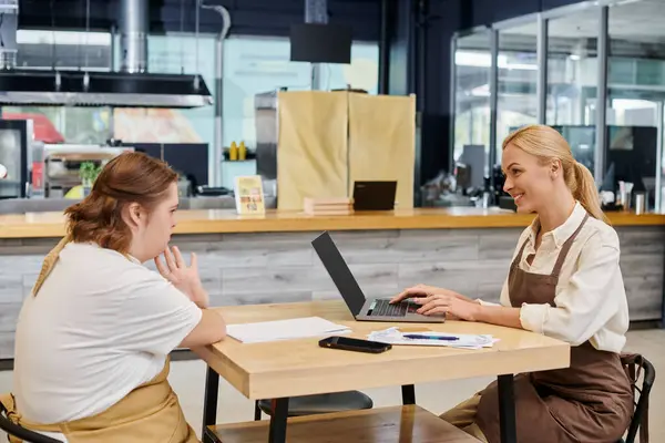 Gestionnaire souriant travaillant sur un ordinateur portable près d'une employée ayant une déficience mentale à la table dans un café — Photo de stock