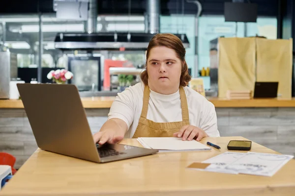 Mujer joven con trastorno mental que trabaja en el ordenador portátil cerca de teléfono inteligente en la mesa en la cafetería moderna - foto de stock