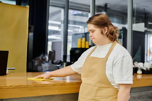 Young female employee with mental disorder working in modern cafe and cleaning counter with rag — Stock Photo