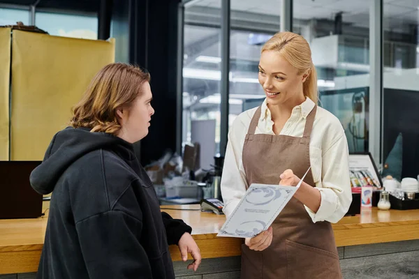 Manager caffè sorridente che mostra la carta di menu per giovane dipendente femminile con sindrome di Down, inclusività — Foto stock