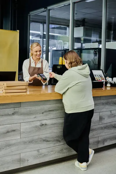 Joven cliente femenino con síndrome de Down con tarjeta de crédito cerca de gerente con terminal en la cafetería - foto de stock