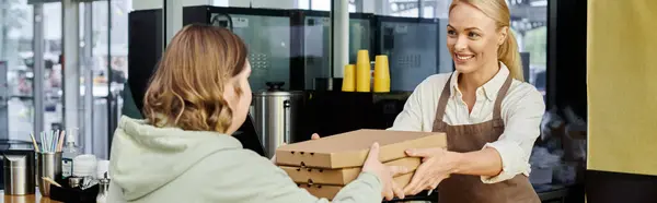 Administrador de café feliz dando cajas de pizza a cliente femenino con síndrome de Down en la cafetería, pancarta - foto de stock
