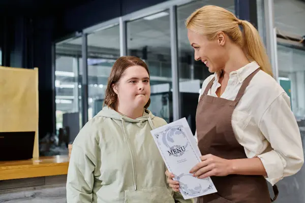 Cheerful administrator holding menu card near thoughtful woman with down syndrome in modern cafe — Stock Photo