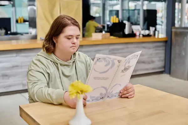 Thoughtful female client with down syndrome looking at menu card while sitting at table in cafe — Stock Photo