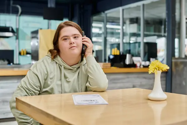 Young woman with down syndrome talking on mobile phone on table in modern cafe, inclusivity — Stock Photo
