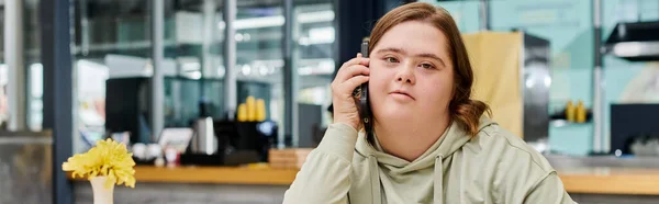 Young woman with mental disability talking on mobile phone in modern and cozy cafe, banner — Stock Photo