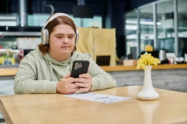 Woman with down syndrome holding smartphone and listening music in headphones in cozy cafe — Stock Photo