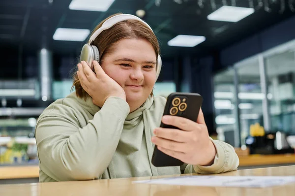 Cheerful woman with mental disorder holding smartphone and listening music in headphones in cafe — Stock Photo