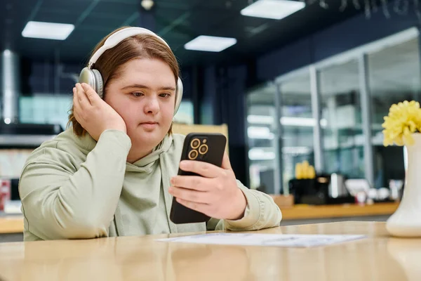 Young woman with mental disability in wireless headphones holding pizza boxes in modern cafe — Stock Photo