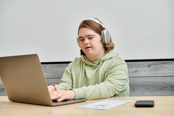 Young woman with down syndrome in wireless headphones networking on laptop at table in modern cafe — Stock Photo