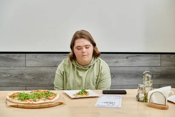 Jeune femme avec un handicap mental regardant délicieuse pizza tout en étant assis dans un café confortable moderne — Photo de stock