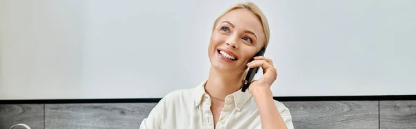 Cheerful blonde woman smiling during conversation on mobile phone in cafe, horizontal banner — Stock Photo
