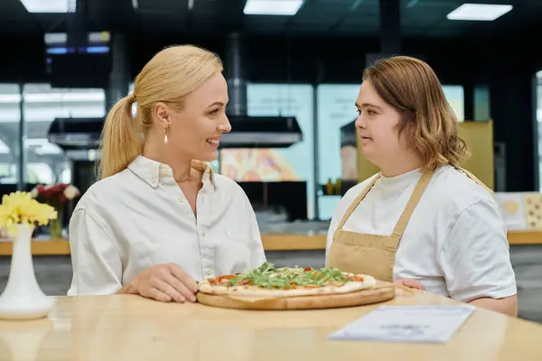 Jeune serveuse atteinte de troubles mentaux servant une délicieuse pizza près d'une femme souriante dans un café moderne — Photo de stock