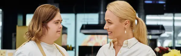 Heureux femme blonde et jeune serveuse avec le syndrome du duvet souriant à l'autre dans le café, bannière — Photo de stock