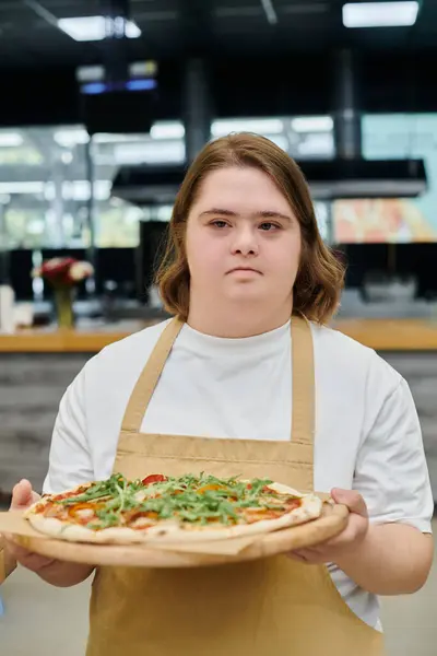 Jovem com síndrome de down segurando deliciosa pizza enquanto trabalhava no café moderno, inclusividade — Fotografia de Stock