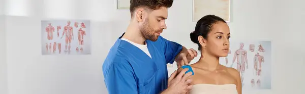 Good looking bearded doctor putting kinesiological tapes on his patient during appointment, banner — Stock Photo