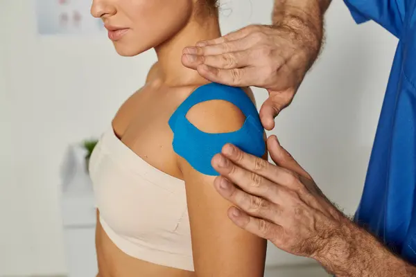 Cropped view of young woman waiting while doctor putting kinesio tape on her shoulder, healthcare — Stock Photo