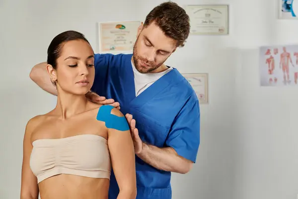 Beautiful woman on appointment while her doctor putting kinesio tapes on her shoulder, healthcare — Stock Photo