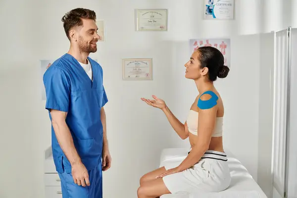 Attractive young woman with kinesio tapes talking to her cheerful bearded doctor, healthcare — Stock Photo