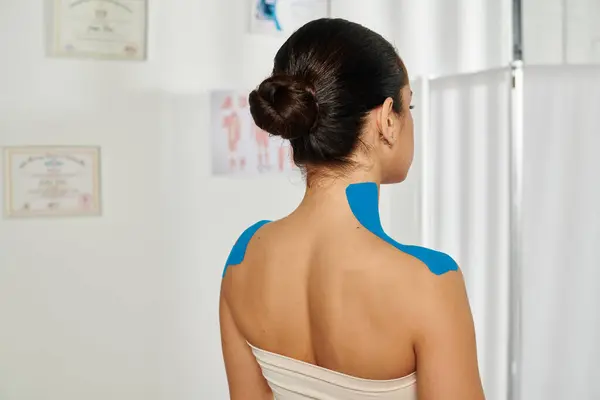 Vista posterior de una paciente joven con cintas kinesiológicas en el cuello y los hombros, atención médica - foto de stock