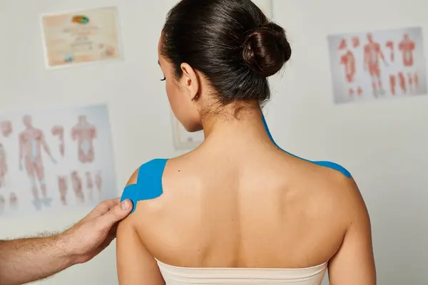 Cropped view of doctor putting kinesiological tapes on shoulder of young attractive female patient — Stock Photo