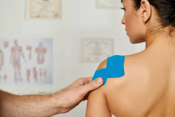 Back view of attractive female patient with hand of doctor that putting kinesio tapes on her body — Stock Photo