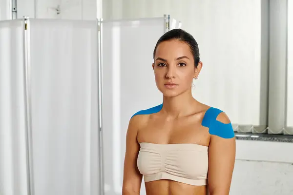 Attraktive junge Patientin mit kinesiologischen Tapes auf den Schultern, die in die Kamera schaut, Gesundheitswesen — Stockfoto