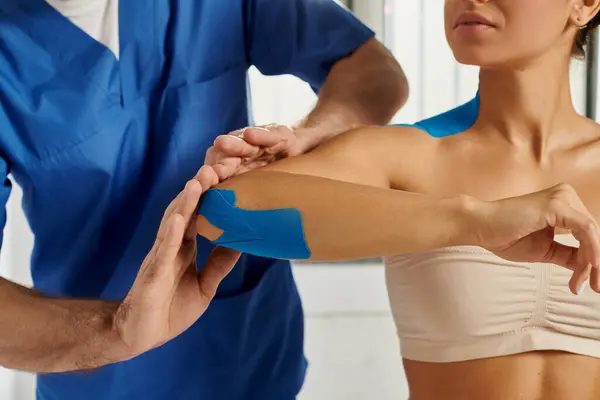 Cropped view of doctor putting kinesiological tapes on elbow of his young patient, healthcare — Stock Photo