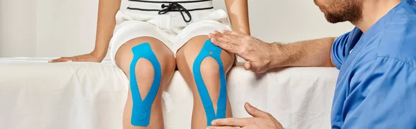 Bärtiger Arzt legt kinesiologische Klebebänder auf das Knie seines Patienten während des Termins, Banner — Stockfoto