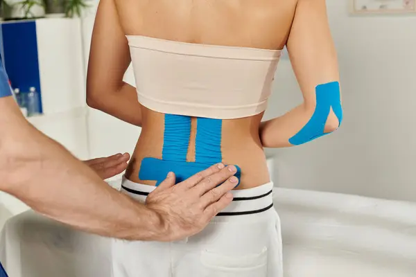 Cropped view of doctor putting kinesiological tapes on back of young female patient, healthcare — Stock Photo