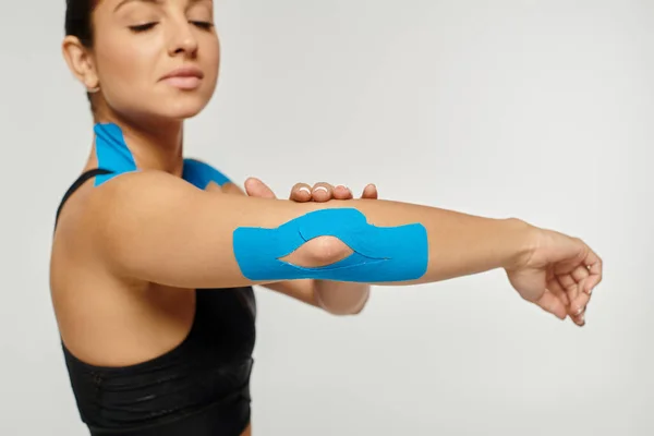 Attractive young woman with kinesiological tapes on her elbow and shoulders on gray background — Stock Photo
