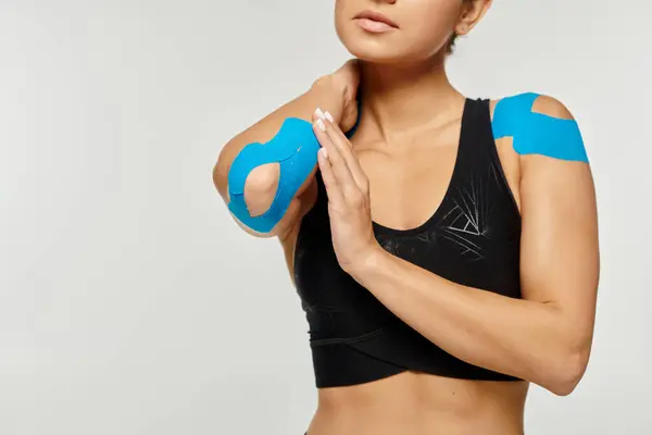 Cropped view of young woman in black sport wear touching her elbow with kinesiological tapes on it — Stock Photo