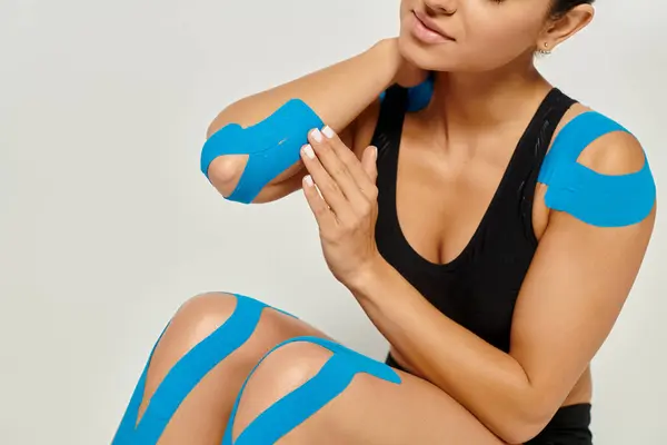 Cropped view of young woman in sport wear sitting on floor touching kinesiological tapes on her body — Stock Photo